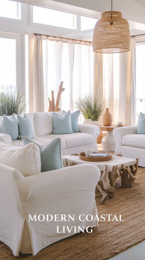 Bright coastal living room with white sofas, jute rug, floor-to-ceiling windows, blue pillows, driftwood decor, rattan light, and potted grasses. Text overlay at the bottom reads Modern Coastal Living. Pottery Barn Inspired Living Room Coastal, Beach Condo Decorating Ideas, Boho Beach Living Room, Beachy Living Room Ideas, Modern Coastal Living Room Ideas, Coastal Casual Living Room, Neutral Coastal Living Room, Coastal Modern Decor, Coastal Living Rooms Ideas