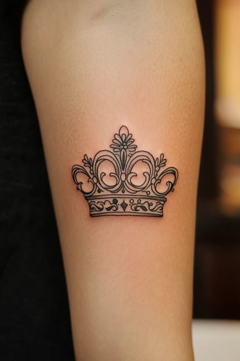 A black outline tattoo of a crown on an upper arm. Biblical Crown Tattoo, Royalty Tattoo For Women, Female Crown Tattoo, Queen Crown Tattoo Design, Simplistic Crown Tattoo, Small Crown Tattoos For Women Queens, Tattoo Ideas Crown Queen, Queen Tattoo For Women, Tiny Queen Crown Tattoo