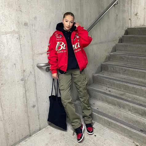 Girl wearing black sweatshirt, red racing jacket with olive green cargo pants. Wearing patent bred Jordan 1s. Holding black tote back. Standing in parking garage. Jordan 4 Bred Women Outfit, Pink Jordan 3 Outfit Women, Jordan 1 Flannel Outfit, Outfits With Patent Bred 1s, Red Jacket Outfit Street Style, Female Streetwear Outfits Winter, Bred 1s Outfit Women, Bred Patent 1s Outfit, Red 1s Outfit