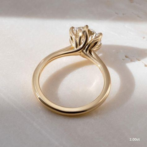 This 2 carat lab grown yellow gold elswin twisted flower engagement ring elevates and enhances the round brilliant cut diamond in a way in which this simple claw prong solitaire features an open basket with six elegant leaves that cradle the center diamond. Handcrafted in Hatton Gardens, London.  ... daha fazla Claw Engagement Ring, Flower Engagement, Minimalist Engagement Ring, Flower Engagement Ring, Claw Prong, Diamond Solitaire Rings, 2 Carat, Round Brilliant Cut Diamond, Solitaire Engagement Ring