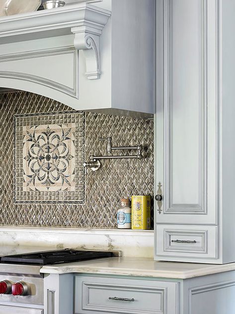 Pair colorful cabinets with a statement kitchen backsplash to create a focal point. In this kitchen, most of the cabinetry is cream color, but pale blue cabinets set the cooktop area apart. Tile above the cooktop provides another visual drawing card, with its textural beauty and an intricate inset design. Trendy Kitchen Backsplash, Recycled Glass Tile, Stove Backsplash, Unique Kitchen Backsplash, Diy Kitchen Backsplash, White Kitchen Backsplash, Kitchen Backsplash Designs, Glass Backsplash, Backsplash Designs