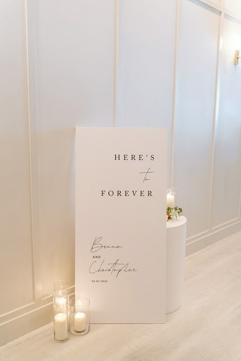 White Here's to forever welcome sign black script Day Of Signage Wedding, Minimalistic Modern Wedding, Wedding Signage Fonts, Wedding Sign Reception, Modern Elegant Wedding Signage, Sinages Design For Wedding, Minimal Wedding Sign, Entrance To Wedding Reception, Wedding Signage Quotes