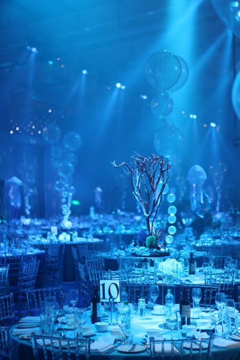 To access the dining area guests made their way through an opulent deep wall of fabric columns, emulating waves and shafts of light in the sea. Dining tables were dressed in four different shades of blue cloths, surrounded with clear perspex chairs. Bubble, coral and internally illuminated jelly fish table centres combined with creative under the sea lighting brought the space to life and left guests utterly in awe as 3mtr jellyfish acrobats danced the night away over the top of the tables. Water Theme Party Decorations, Under The Sea Debut Theme, Under The Sea Party Theme Decoration, Ocean Theme Event, Under Water Theme Decorations, Under The Sea Themed Wedding, Quince Under The Sea Theme, Atlantis Decorations Theme Parties, Under The Sea Theme Wedding