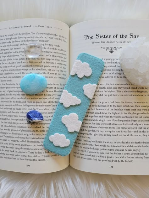 A light blue bookmark with white clouds sitting ontop of a book, surrounded by crystals. Easy Felt Patterns, Book Marks Felt, Felt Tea Bag Bookmark, Bookmark Clouds, Kids Bookmark Craft, Small Felt Projects, Diy Felt Bookmarks, Felt Bookmarks Diy Pattern, Bookmark Handmade Ideas