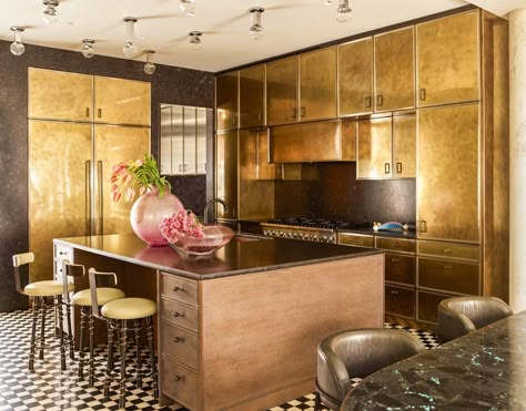 Kelly Wearstler Kitchen Design • The kitchen cabinets, hood and refrigerator are all clad in patinated brass, giving the subterranean room a warm glow. A pair of snake barstools were custom made for the space and nestle underneath a generous, marble-topped center island, which also holds a handcrafted footed bowl by Ettore Sottsass for Bitossi. Sources of light are all set in the ceiling, and include opaline hand-blown glass pendant lights in the style of Wiener Werkstatte. #kellywearstler Golden Kitchen, Kelly Wearstler Interiors, Wine Aesthetic, Modern French, New York Life, Kelly Wearstler, Interior Kitchen, Top Interior Designers, Products Ideas