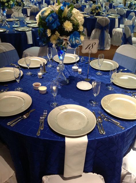 Royal blue pin-tuck table toppers, silver chargers, white chair covers, white napkins, sheer royal blue chair sashes Royal Blue Gold And White Wedding Table Settings, Blue And Silver Table Decorations, Royal Blue Centerpieces Quinceanera, Royal Blue Quince Theme, Table Decorations Blue, Royal Blue Chair, Wedding Table Decorations Blue, Royal Blue Centerpieces, Blue Quinceanera Theme