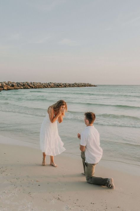 Young couple dressed in white & neutral summer clothing - on shore of beach in St Andrews State Park, PCB Florida.  Young man is kneeled down on one knee, with ring outstretched, girl is excitedly covering her face with her hands. Photo taken by intimate wedding & portrait photographer Brittney Stanley of Be Seen Photos Simple Proposal Ideas Beach, Beach Engagement Surprise, Surprise Beach Engagement, Surprise Proposal Photoshoot Beach, Marriage Proposal Beach, Engagement At The Beach, Florida Proposal Ideas, Engagement Proposal Ideas Beach, Proposal Beach Photos