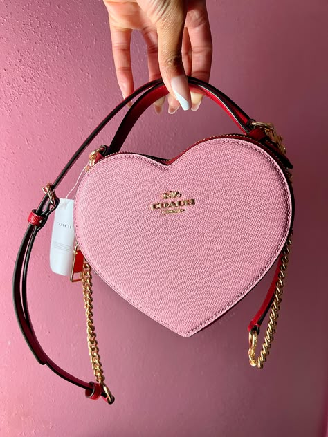 The Coach Heart Bag is the new it bag that recently dropped at the Coach Outlets. It's hard to find, but check out my blog to see how I was able to get one! Coach Bags Heart, Heart Coach Purse, Pink Coach Bag Aesthetic, Coach Valentine Bag, Coach Heart Bag Outfit, Heart Coach Bag, Coach Heart Purse, Coach Handbags Outfits, Pink Luxury Bag