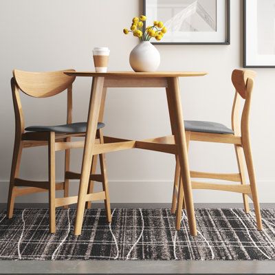 Inspired by iconic mid-century silhouettes, this 3-piece dining set creates a cohesive and minimal look in your kitchen or dining room. It includes a counter-height table and two stools, all crafted from solid and engineered wood with a light, natural oak finish that complements any modern space. The table is built on top of splayed legs with X-shaped support, and its round table top is designed to accommodate two guests after assembly. Both stools showcase curved backrests and built-in footrest Small Round Kitchen Table, Modern Kitchen Stools, Small Round Dining Table, Small Dining Sets, Round Kitchen Table, Small Kitchen Tables, Small Apartment Kitchen, 3 Piece Dining Set, Round Kitchen