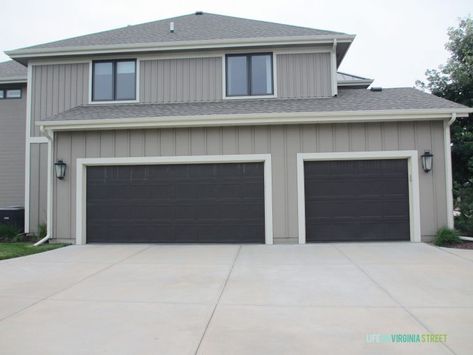 The garage doors are already dark, and could work in place of a true black Black Garage Door Gray House, Tan House With Black Garage Doors, Charcoal Gray Garage Door, Peppercorn Garage Door, Dark Gray Garage Door, Black Garage Doors Grey House, Gray House Black Garage Door, Dark Grey Garage Door, Dark Brown Garage Doors