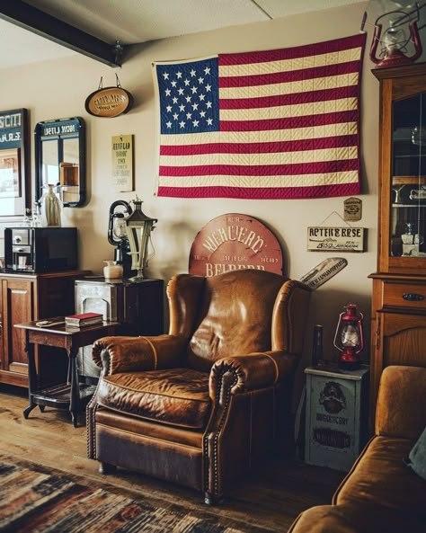 A cozy living room with vintage Americana decor, featuring a worn leather armchair, a quilted American flag on the wall, antique wooden furniture, and nostalgic memorabilia like old signage and rustic lanterns #americana #vintage #decor #rustic #nostalgic #antique Vintage Camp Interior Design, Western Americana Decor, Vintage Country Home Decor, Vintage Americana Room, Americana Cabin, American Flag Room, Vintage Lodge Decor, Americana Living Rooms, Americana Room