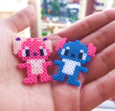 Uma mão cor de pele clara aberta, segurando dois bonecos, um da Angel(rosa e rosa claro) e um do Stitch(azul e branco) do filme Lilo & Stitch, feito de hama beads ou perler beads, que são como bolinhas, para fazer artesanato, formas, personagens, etc. Perler Beads Stitch, Hama Disney, Beads Stitch, Mini Hama Beads, Angel Stitch, Melty Bead Designs, Beads Perler, Melt Beads Patterns, Modele Pixel Art