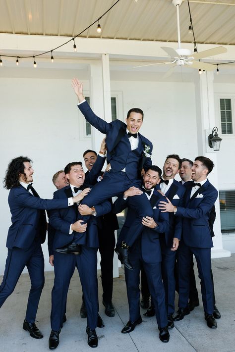 The couple wanted the wedding party to complement the environment of the venue in a timeless and upscale way that reflected the blue lake and beautiful surrounding greenery. The bridesmaids wore dusty blue Azazie dresses with soft, natural glam by LJ Artistry and Reborn Hair Company, and carried bouquets full of soft green, soft pinks, and creams. The groomsmen wore navy blue suits with black lapels and bowties from Men's Wearhouse. #lakewedding #groomsmen Wedding Groomsmen Attire Navy Blue, Cobalt Blue Groomsmen Attire, Groomsmen Attire Navy And Grey, Blue Tuxes Wedding, Navy Tux Groomsmen, Navy Black Tie Wedding, Blue Suits Bridal Party, Dark Blue Summer Wedding, Blue Tuxedo Wedding Groomsmen