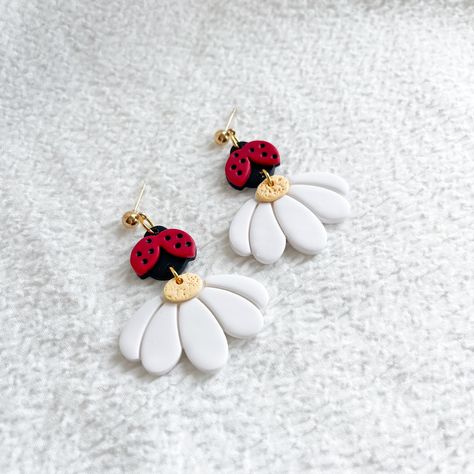 These charming earrings feature the delightful combination of vibrant ladybugs and delicate daisies, meticulously crafted from high-quality polymer clay. Perfect for nature lovers and those who appreciate unique, handcrafted jewelry, these earrings are sure to bring a smile to your face and a pop of color to your look. Measurements: 2.00 in. x 1.50 in. Gold stainless steel ball posts. Hypoallergenic. All earrings are handmade. Please expect some variations/imperfections. Processing Information All orders ship in 3 business days. Your order will arrive after the processing time + ship time. Creative Polymer Clay Earrings, Polymer Clay Bookmark Ideas, Fimo Clay Jewelry, Simple Clay Earrings, Clay Ladybug, Clay Experiments, Cute Polymer Clay Earrings, Polymer Clay Fruit, Earring Art