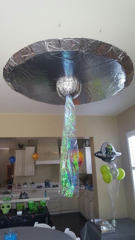 UFO / alien spaceship decoration made from foam board, duct tape, spray adhesive, tin foil, Styrofoam ball, battery operated strobe light, cellophane. hung with command hooks and fishing line. Spaceship Party Space Theme, Savory Space Themed Food, Spaceship Decorations Diy, Alien Spaceship Decoration, Alien Themed Decorations, Diy Alien Decor, Spaceship Theme Party, Sci Fi Birthday Party, Space Photo Backdrop