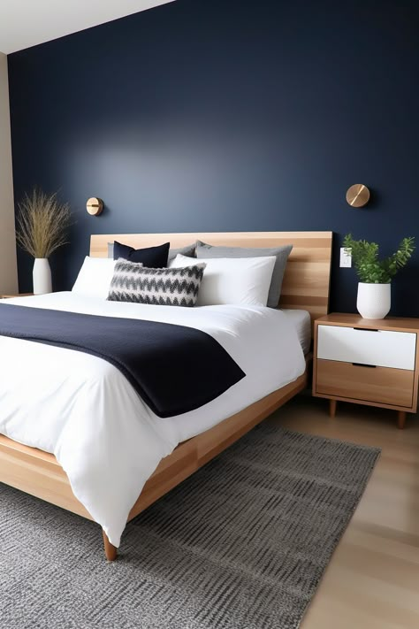 Photographed from an angle that captures the entire king-size bed and most of the room, this modern bedroom features a midnight blue accent wall balanced by light wood tones. A wooden headboard, matching nightstands, and a neutral area rug complete the look. Blue Feature Wall Bedroom, Midnight Blue Bedroom, Blue Feature Wall, Dark Blue Bedrooms, Navy Blue Bedrooms, Blue Bedroom Walls, Feature Wall Bedroom, Blue Accent Walls, Dekorasi Kamar Tidur