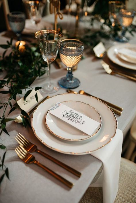 Bisous Events - table setting - vintage plates, gold cutlery, grey-blue water goblet, gold-rimmed wine glass and base ball tickets as a wedding favour! #vintageplates #greenery #garland #weddingfavours #bisousevents #torontoweddingplanner #goldcutlery #tablesetting #weddingdetails #weddingdecor #weddinginspiration #wedding #weddingdesign #watergoblets #wedding #bohowedding Gold Cutlery Table Setting Wedding Ideas, Blue And Gold Plate Setting, Classy Dinner Table Setting, Cutlery Set Up On Table, Water Glasses Table Setting, Vintage Glass Table Setting, Cutlery Setting Table, Gold Plates Table Setting, Classy Table Settings