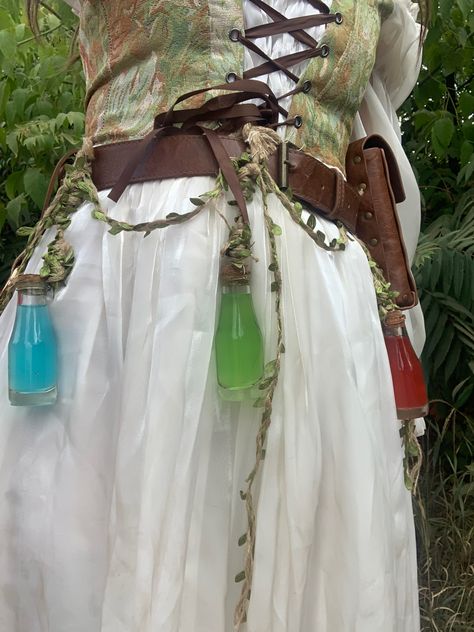 Green corset over white dress with hanging potions Potion Seller Costume, Ren Faire Fairy Accessories, Ren Faire Outfits Accessories, Fantasy Apothecary Outfit, Trinket Fairy Costume, Green Fairy Ren Faire, Ren Fair Elf Costume, Ren Faire Corset Outfit, Ren Faire Goblin