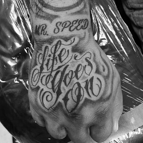 Shaded Script Hand Life Goes On Tattoos For Males Life Goes On Hand Tattoo, Life Goes On Tattoo Design, Life Goes On Tattoos, Giver Tattoo Ideas, Giver Tattoo, Such Is Life Tattoo, Hand Tattoos For Guys Words, Life Is Good Tattoo, Life Goes On Tattoo Ideas