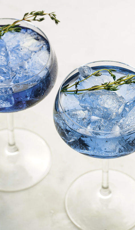 This ready-to-serve wine cocktail gets a little effervescent boost with the addition of tonic water. Serve in a coupe glass for a stunning sky-blue cocktail that’s fresh, fruity and lightly sweet. Ice Themed Cocktails, Beach Themed Drinks Cocktails, Blue And Green Cocktails, Pretty Cocktail Glasses, Blue Pea Flower Cocktail, Ocean Breeze Cocktail, Ocean Cocktail Drinks, Elegant Drinks, Blue Glitter Cocktail