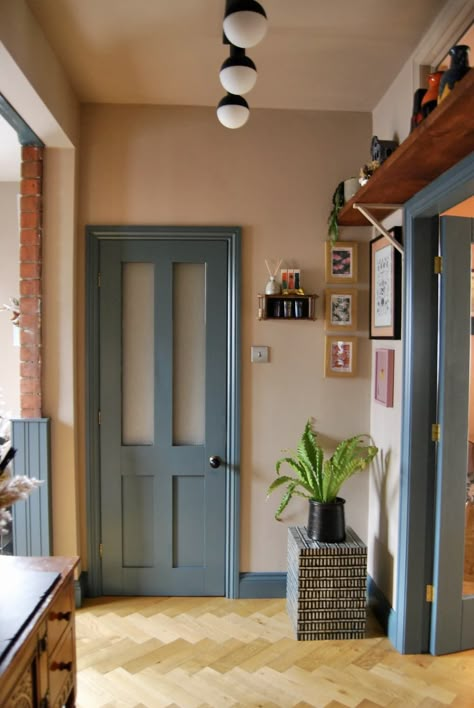 The doorway to a kitchen with a blue-trim accent next to a small gallery wall of framed art. Inchyra Blue Woodwork, Colour Door Frame, Eclectic Accent Wall Ideas, Blue Painted Interior Doors, Teal Trim Interior, Colorful Moldings And Trim, Creative Wainscoting Ideas, Contrast Door Frame, Color Trim And Doors