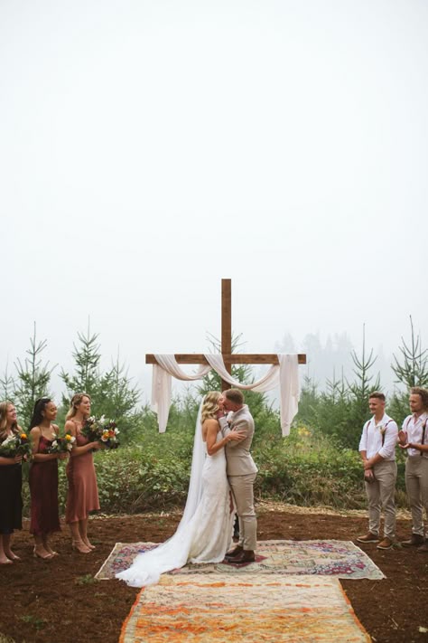 We built this cross using 12ft 2x4 and 6ft 2x4. I stained it with “Early American” wood stain and then we cemented it into the ground. The fabric is from Jo~Anne’s fabric. Wedding Cross With Drape, Yellow Stone Wedding, Diy Wooden Cross Wedding, Cross For Outdoor Wedding, Cross Outdoor Wedding, Bride On Right Side Of Alter, Wooden Cross Wedding Backdrop, Cross Arbor For Wedding, Wedding Wooden Cross