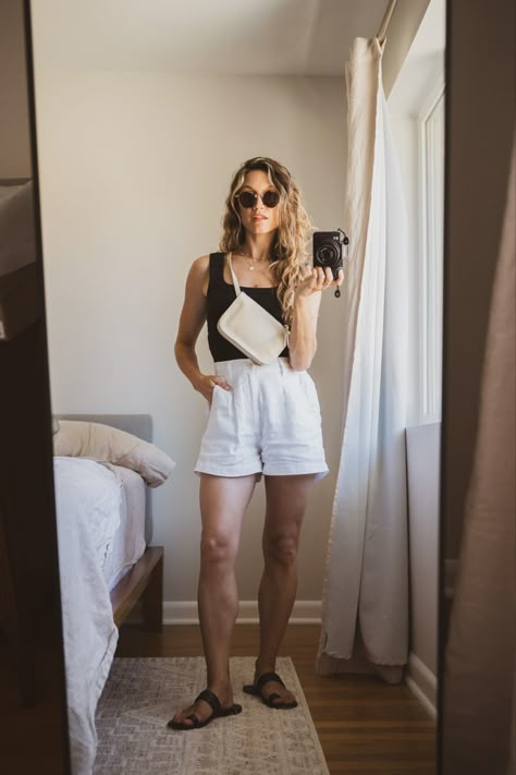 Ashley wearing a black tank, white linen shorts, black sandals, a beige belt bag, and tortoiseshell sunglasses Outfit With Linen Shorts, Olive Linen Shorts Outfit, Linen White Shorts Outfit, White Shorts Black Top Outfit, Styling Linen Shorts, Cream Linen Shorts Outfit, Black Sandals Outfit Casual, Summer Linen Shorts, White Linen Shorts Outfit Summer