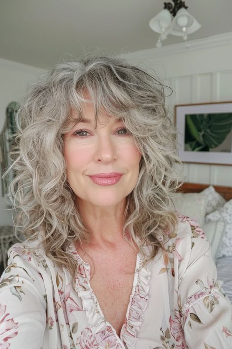 Smiling woman with curly gray hair wearing a floral blouse in a cozy, well-decorated room. Gray Curly Shag Hairstyles, Curl Shag Hairstyles, Curly Gray Hair With Bangs, How To Do Bangs With Curly Hair, Hair Inspiration With Bangs, Fine Curly Hair With Bangs, Bangs For Curly Hair Natural Curls, French Bangs Curly Hair, Curly Hair Fringe Bangs