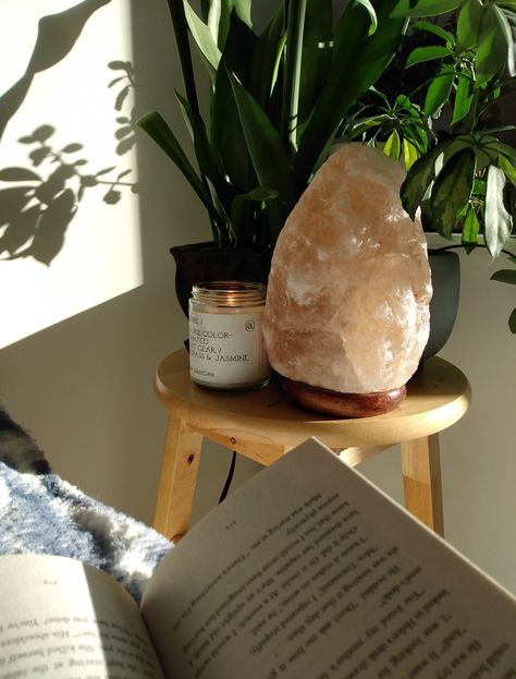 Book open on a cozy chair with a bright, cozy and aesthetic wooden side table with plants, a salt lamp and a lit candle. There is sunlight on the wall. Cozy, warm, aesthetic and bright room inspo & decor. Candle Office Ideas, Therapy Aesthetic Room, Salt Lamp Room, Feminine Aesthetic Home, Girl Apartment Aesthetic, Salt Lamp Aesthetic, Therapist Office Aesthetic, Chill Vibes Aesthetic, Glass Oil Diffuser