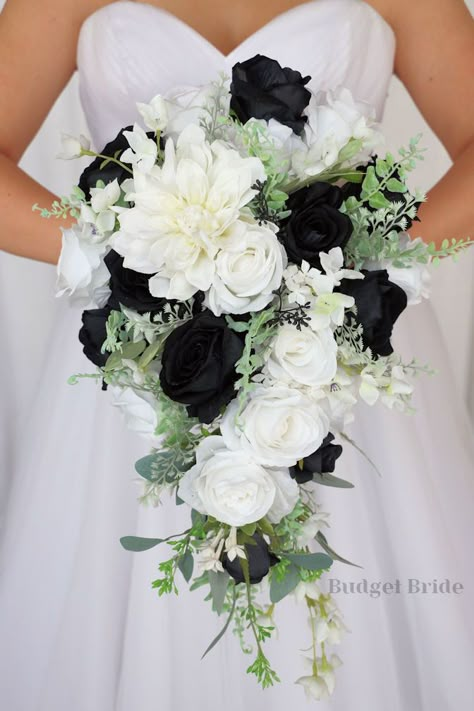 This is a cascading brides bouquet with white dahlia, white and black roses and greenery. All of our wedding bouquets are made with artificial wedding flowers. Wedding Black And Greenery, White Roses Bridal Bouquet With Greenery, Black And Sage Wedding Bouquet, Black Wedding Floral Arrangements, Modern Black And White Wedding Bouquet, White And Black Bridesmaid Bouquet, Black White And Green Wedding Bouquet, Wedding Flowers For Black Dresses, Black And White Wedding Bride And Groom Table