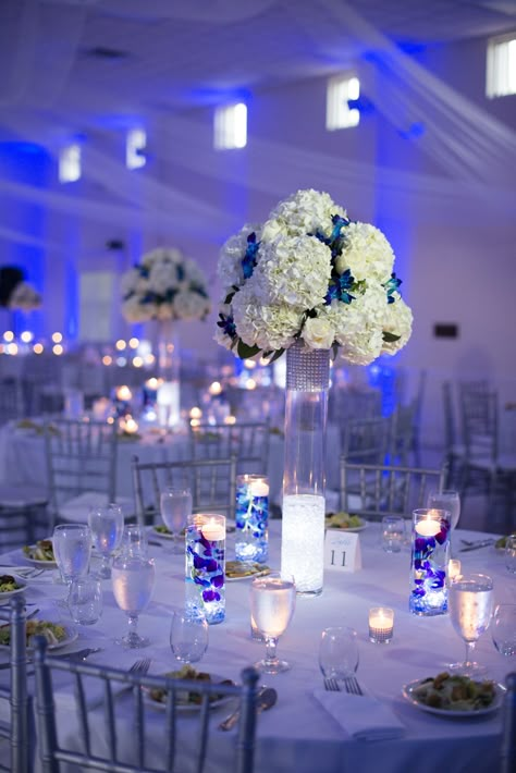 White and Silver Reception Decor with Blue Uplighting Wedding Decorations Blue, Silver Wedding Centerpieces, Blue Uplighting, Royal Blue Wedding Theme, Silver Wedding Theme, Royal Blue Quinceanera, Blue Wedding Receptions, Uplighting Wedding, Quinceanera Centerpieces