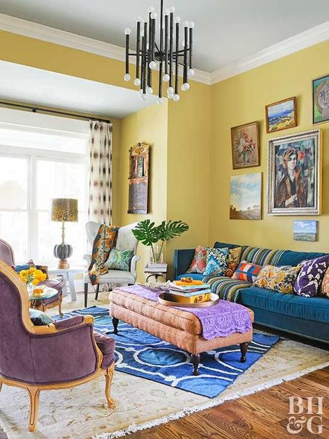 Yellow is one of many colors featured in this eclectic living room. The yellow walls host a gallery of colorful art, and a pacific blue sofa holds plenty of patterned pillows. Layered rugs soften the space, while yellow living room accessories, like fresh flowers, a lampshade, and throw pillows, incorporate the sunny color scheme throughout. Yellow Living Room Accessories, Yellow Walls Living Room, Yellow Decor Living Room, Yellow Wall Decor, Walls Living Room, Yellow Room, Yellow Living Room, Living Room Color Schemes, Yellow Decor