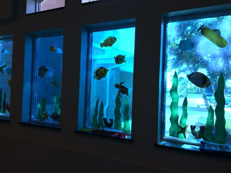 Window panels created with blue cellophane rolls, fish cutouts and seaweed made from bulletin board paper. Fish Window Display, Underwater Window Display, Aquarium Classroom Decorations, Daycare Room Ideas, Under The Sea Classroom, Ocean Vbs, Breaker Rock Beach, Scuba Vbs, Underwater Party