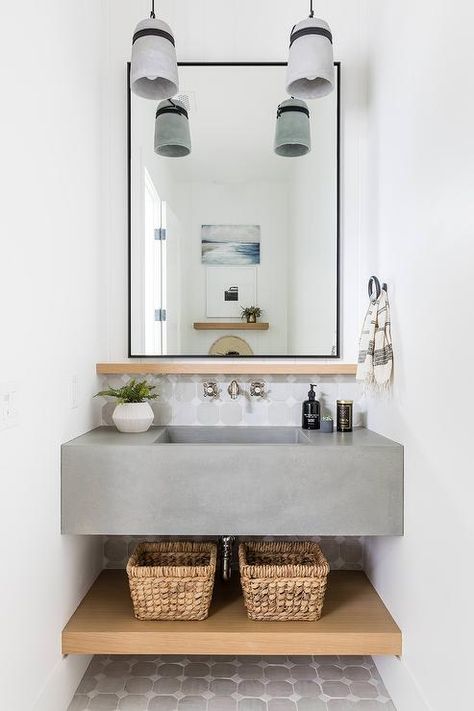 Powder room features a floating concrete sink vanity with a nickel faucet mounted on white and gray tiles under a black rectangular mirror, woven baskets and white and gray floor tiles, illuminated by glass lanterns. Boston Condo, Update Small Bathroom, Cement Sink, Salt Interiors, Small Half Bathroom, Concrete Vanity, Pure Salt Interiors, Keys House, Floating Sink