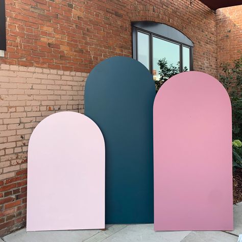 Photo shows three wooden arches of various sizes and colors propped against a brick wall. The far left arch is the shortest and is blush pink. The middle arch is a dark teal green and is the tallest arch. The far right arch is a middle tone pink mauve. Diy Tinsel Jacket, Diy Photo Backdrop Ideas, Photoshoot Backdrop Ideas, Diy Arches, Chiara Arched Backdrop, Diy Chiara Backdrop, Wedding Ceremony Backdrop Diy, Diy Tinsel, Photo Backdrop Ideas