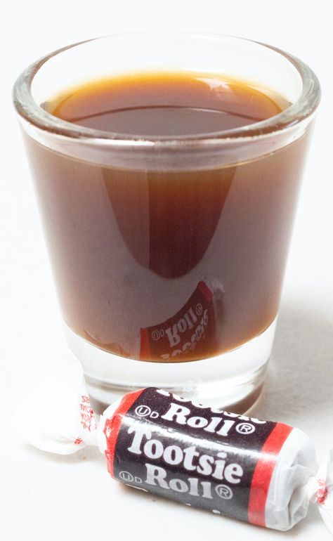 A shot glass filled with a brown tootsie roll shot on a white background next to a piece of tootsie roll candy. Tootsie Roll Shot Recipe, Circus Drinks, Tootsie Roll Drink, Tootsie Roll Shot, Mixology Recipes, Spring Drink, Cocktail Shots, Two Ingredient, Non Alcoholic Cocktails