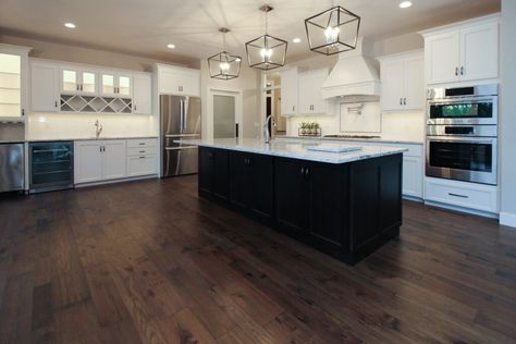 Dark brown hickory hardwood in white kitchen with white tile backsplash and black kitchen island. Black Kitchen Island With Dark Wood Floors, Black Island Dark Floors, Black And White Kitchen Dark Floor, Dark Cabinets With Dark Floors, Dark Wood And White Kitchen, White Kitchen Dark Island, Dark Brown Floor Kitchen, Dark Wood Floors In Kitchen, Kitchen With Dark Wood Floors