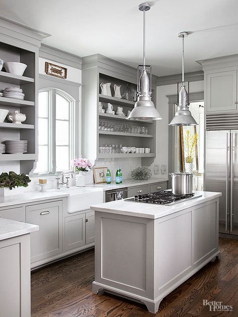 The kitchen's versatile gray base hue coats cabinetry and the island alike while also serving practical purposes. Not only does the neutral color provide more depth than an all-white space, but it also visually enlarges the compact kitchen. Grey Kitchen Table, Light Grey Kitchen Cabinets, Warm Wood Flooring, Light Grey Kitchens, Light Gray Cabinets, Neutral Kitchen, Gray Kitchen, Compact Kitchen, White Marble Countertops