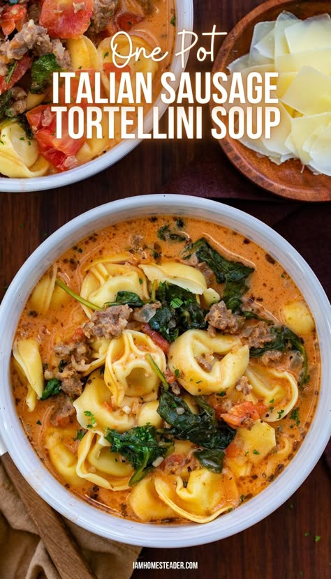 A white bowl filled with Italian Sausage Tortellini Soup, next to it, a second bowl of soup and a wooden bowl of shaved parmesan cheese. Tortilla Sausage Soup, Tortellini Soup With Sausage And Arugula, 30 Minute One Pot Creamy Italian Sausage Tortellini Soup, One Pot Italian Sausage Tortellini Soup, Italian Sausage Tortilla Soup Recipe, Rustic Tortellini Soup Italian Sausages, Tortelinni Soup With Italian Sausage, Creamy Sausage Tortellini Soup Stovetop, One Pot Sausage Tortellini Soup