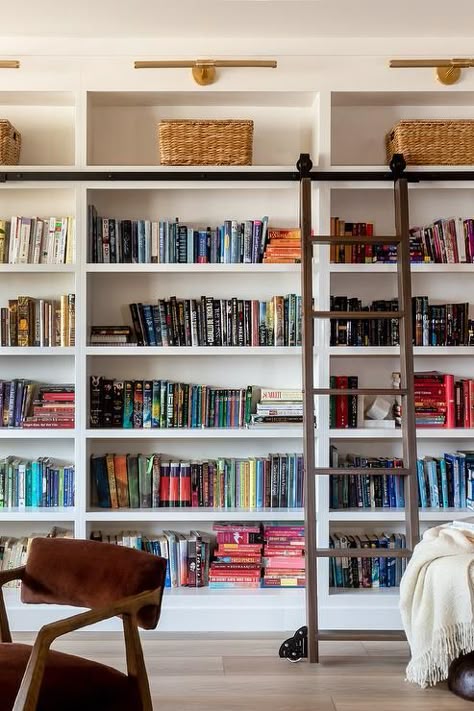 A ladder on rails complements floor-to-ceiling built in bookcases lit by brass picture lights. Modern Manor, House Of Jade Interiors, Summer Room Ideas, Farmhouse Bookshelf, Built In Bookcases, Vibey Apartment, Floor To Ceiling Bookshelves, Den Library, Industrial Farmhouse Decor