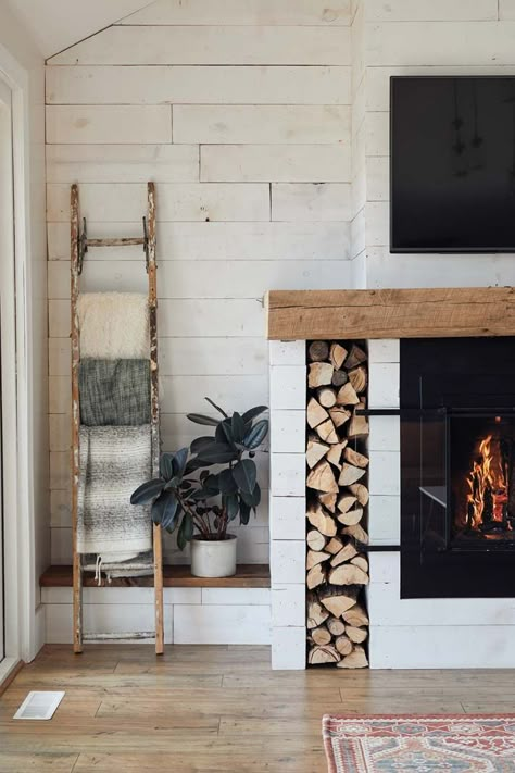 Revamp your fireplace mantel with a farmhouse-inspired look like this one in Kate and Tony Becker’s Corcoran home. Using barn wood adds character and charm, while throwing a blanket ladder, shiplap panels, and built-in firewood holder into the mix ties a simple, stylish aesthetic into your home. Photo by Wing Ta. Fireplace With Space For Wood, Fireplace Blanket Ladder, Blanket Ladder Fireplace, Blanket Ladder Next To Fireplace, Wood Holders For Fireplace, Wood Holder In Fireplace, Built In Wood Box Next To Fireplace, Wood By Fireplace, Firewood Storage Built In Fireplace