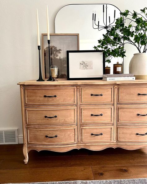 A vintage wood dresser with vintage black handles is pushed against a white bedroom wall. A large plant in a white pot, a stack of two books, a couple of pictures, and two black candlesticks with white candles are placed in front of a large mirror on the dresser. A grey rug is laid on the warm wood floor. Wardrobe Decoration, Dresser Styling, Room Wall Decor Bedroom, Black Candlesticks, Warm Wood Flooring, Bedroom Wall Decor Ideas, White Wall Bedroom, Black Dresser, Oven Cleaner