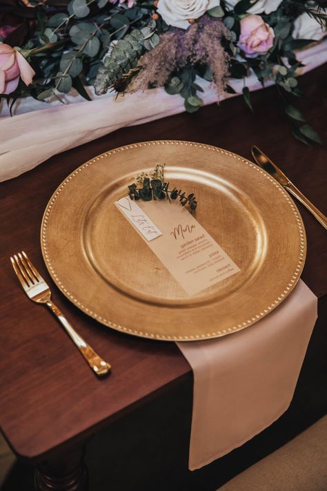 Wedding place setting with gold charger and menu on top. Pink napkin underneath charger with fork and knife on either side. Wedding Menu Charger Plate, Table Setting Gold Charger, White Plates With Gold Chargers, Gold Charger Clear Plate Place Settings, Menu On Charger Plate, Wedding Plate Setting Cheap, Charger Plate With Napkin, Charger Only Place Setting, Party Plate Setting Ideas