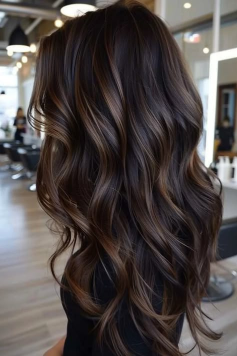 Long, wavy brown hair with caramel highlights in a modern salon setting. Black Hair Mocha Highlights, Darkest Brown Hair With Lowlights, Toning Highlights Darker, Highlights For Dark Brown Hair To Blend Gray, Dark Brunette Lowlights, Brown Black Hair Balayage, Brown And Black Balayage, Black Hair With Brown Lowlights, Shades Of Brown Hair Color Chart