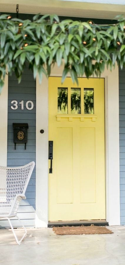 This bright yellow front door uses a coat of Upbeat from BEHR to add color and style to the exterior of this home. A bright white trim and darker blue gray siding complement the vivid color of this front door. Check out the rest of this post from the team at Style Me Pretty to find plenty of front door inspiration. Soft Yellow Front Door, Grey House With Yellow Door, Pale Yellow Door, Pale Yellow Front Door, Yellow Exterior Door, Gray Front Door Colors, Yellow Front Door, Style Curator, Victorian Front Doors