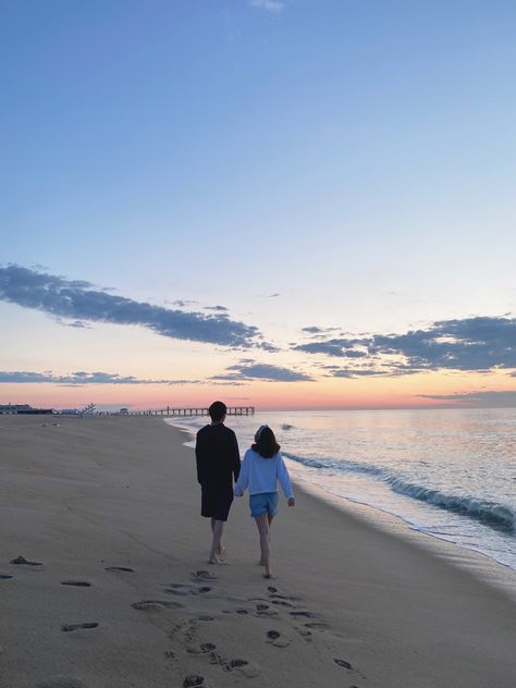 A couple is walking down the shore during sunrise. There are cotton candy skies + a boardwalk in the background Picture Sweet Couple, Beach Dating Aesthetic, Relationship Beach Aesthetic, Morning Date Aesthetic, Sweet Pictures Of Couples, Couple Things To Do Aesthetic, Beach Dates Couple, Beach Date Aesthetic Couple, Sweet Life Aesthetic