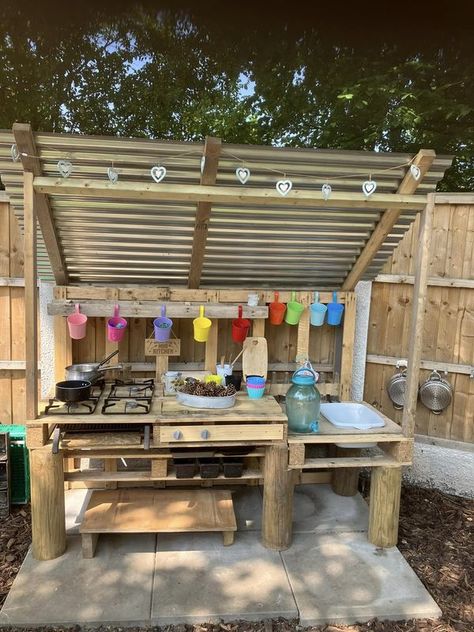 Mud Kitchen Play | We built a mud kitchen in the garden and added a corrugated roof to protect from the elements - it’s been a real hit and the children use scissors t... | Facebook Mud Kitchen With Roof, Painted Mud Kitchen, Mud Kitchen For Kids Pallets, Pallet Mud Kitchen, Kid Backyard, Kids Garden Play Area, Kids Garden Play, Eyfs Outdoor Area, Corrugated Roof