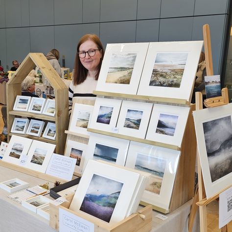 artist standing in front of display of scottish art prints How To Display Canvas Art At Craft Show, Print Display Ideas, Art Market Booth, Art Booth Display, Art Show Display Ideas, Art Market Display, Selling Photography Prints, Art Festival Booth Display, Art Display Ideas