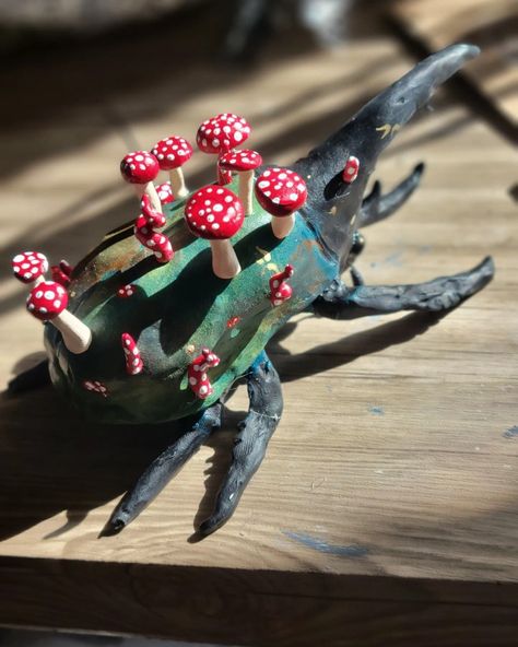 Large beetle with black head, black legs, and green body, facing away from camera, topped with red and white spotted mushrooms. Small gold flecks are scattered across the beetles body, some in the shapes of fae folk wings Paper Mache Beetle, Polymer Clay Beetle, Ceramic Beetle, Bug Ceramic, Clay Beetle, Clay Insects, Ceramic Bug, Weird Sculptures, Clay Bugs