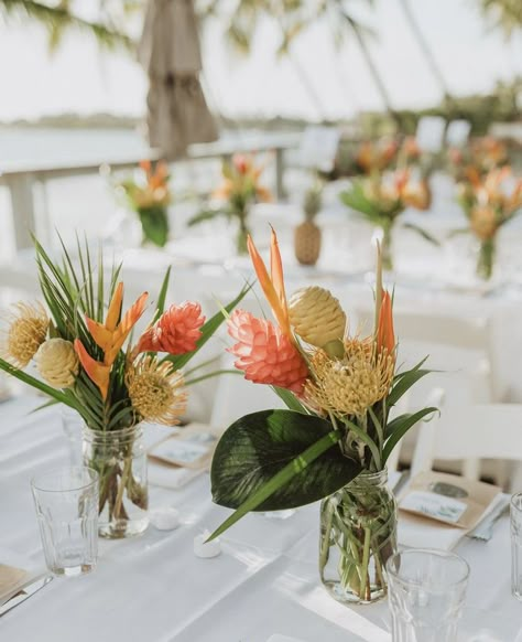 Tropical Floral Arrangements Simple, Tropical Floral Table Arrangements, Waimea Falls Wedding, Mason Jar Tropical Centerpieces, Tropical Flower Table Arrangements, Classy Tropical Theme Party, Railing Decorations Party, Hanging Flower Lights, Small Tropical Floral Arrangements